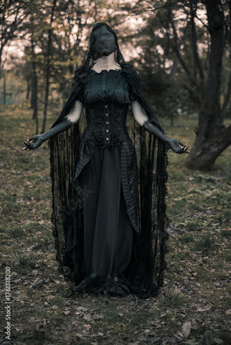 A creepy monster or the ghost of a witch woman with blackened hands and a face wrapped in black bandages in an antique dress with a corset. The Forest witch or the spirit