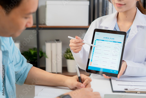 Fotografie Close up nutritionist using tablet to explaining personalized meal plan with AI to patient during healthcare consultation, healthy lifestyle, woman dietitian showing nutrition plan with AI on tablet
