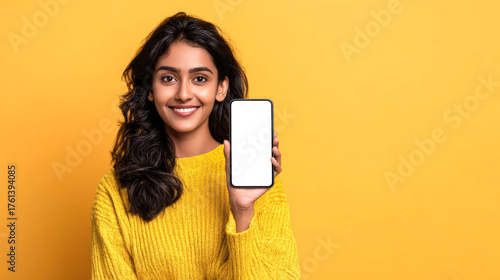 A smiling Indian woman in a sweater holds a smartphone with a blank screen against a yellow background. A beautiful young woman shows a phone with a white screen