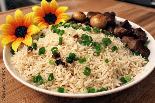 A beautifully presented rice dish garnished with fresh green onions, accompanied by savory meat and mushrooms, adorned with bright yellow flowers for an appealing and vibrant touch