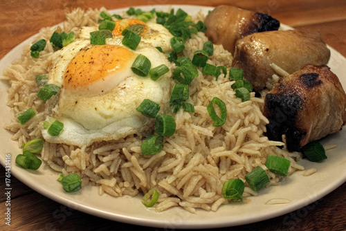 A hearty dish featuring flavorful rice topped with sunny-side-up eggs and paired with savory grilled pork, garnished with fresh green onions.