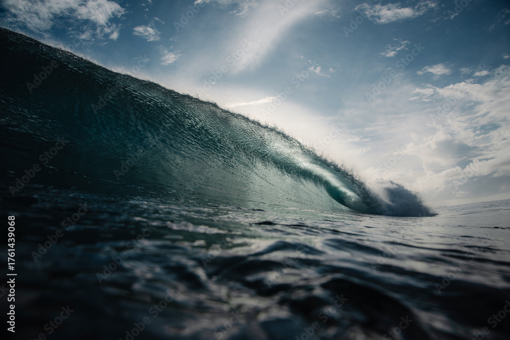 Fototapeta premium A powerful ocean wave curls into a barrel as it breaks under a dramatic, sunlit sky.