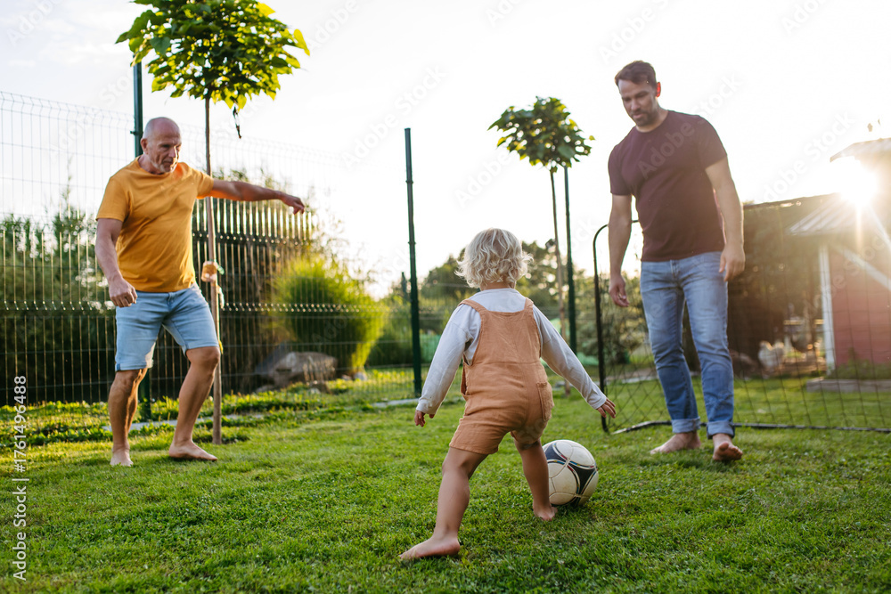 Obraz premium Little boy playing football with father and grandfather in backyard.