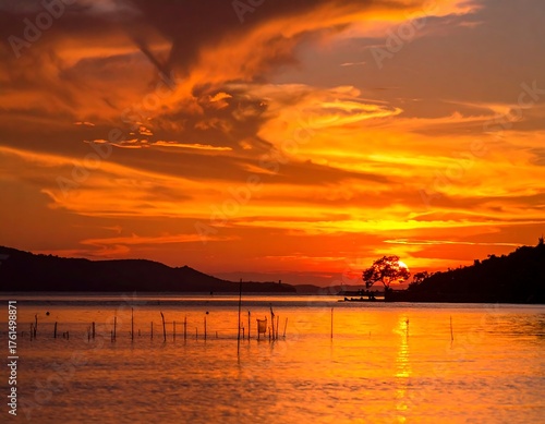 Fiery sunset over a calm lake reflecting orange hues and silhouettes