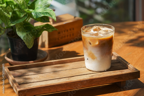 a glass of iced milk coffee on wooden table in sun light and shade