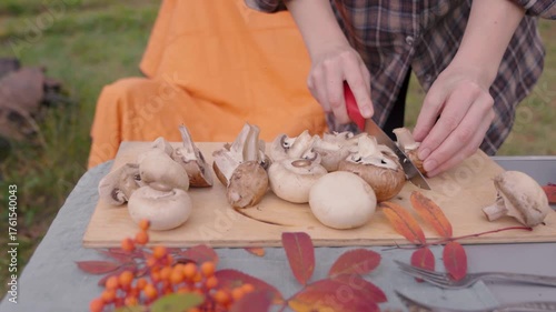 A woman enjoys a serene picnic in nature during autumn as she skillfully slices various types of mushrooms. The peaceful atmosphere is enhanced by vibrant fall colors and a soft breeze.