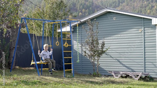 A young boy plays joyfully on a swing set in a backyard surrounded by trees and a blue fence. The sun shines brightly on a clear day, creating a cheerful atmosphere for outdoor fun.