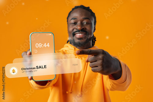 Man shows smartphone with Christmas sale notification against bright orange background