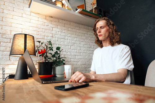 Young man working on laptop in cozy home office with plants and warm lighting