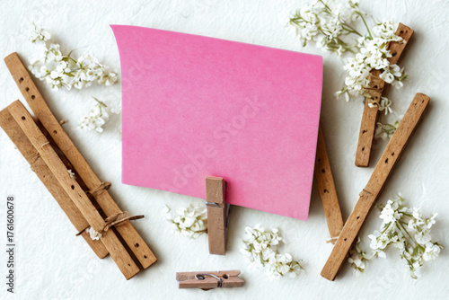 Pink paper note held by clothespins surrounded by flowers and wood