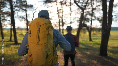 Wallpaper Mural Back view of man hiking trail with yellow backpack in forest. Morning sunlight through trees creates soft shadows. Nature walk in peaceful forest trail. Outdoor travel backpack and hiking journey Torontodigital.ca