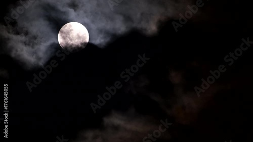 Full moon in dark night sky with ominous foreboding clouds passing by, telephoto