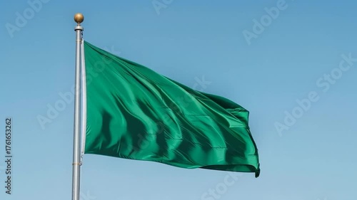 Green flag is waving against a blue sky background