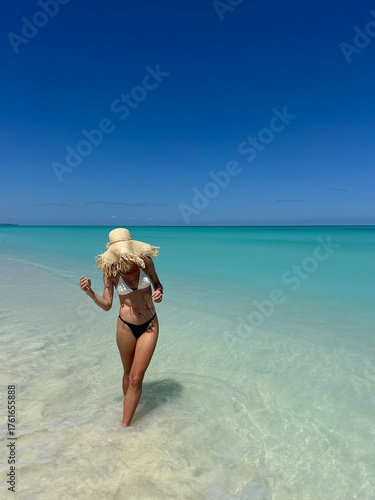 A woman standing on a beautiful tropical beach in Madagascar with clear turquoise water and white sand. The bright sunlight, blue sky, and crystal-clear ocean create a peaceful and exotic summer 