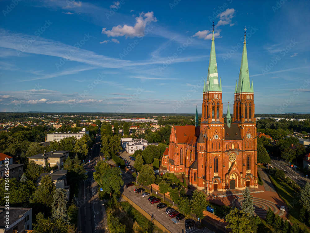 Obraz premium Aerial view historic Basilica Saint Anthony Rybnik, Poland, vertical composition, evening sunlight, neo-Gothic brick architecture, twin towers, urban park, tourism, editorial use