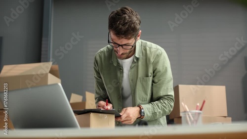 A man is sitting at a desk with a laptop and a clipboard
