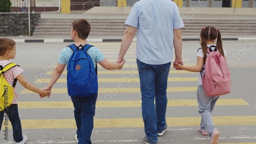 Group of students with dad, Early school drop off, Safety first at crosswalk, Children united with parent, School day starts, Colorful backpacks, Street safety awareness, Pedestrian family crossing