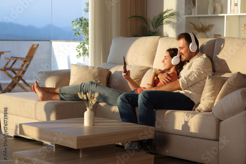 Happy couple sharing music checking phone on a couch