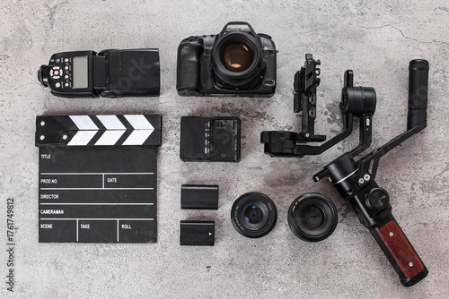 Flat Lay Of Filmmaker Gear With Camera, Gimbal, Clapperboard, Lenses, Flash Over Cement Background