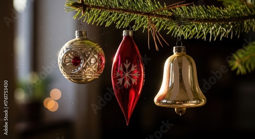 Assorted christmas tree ornaments hanging from a pine branch with warm lighting