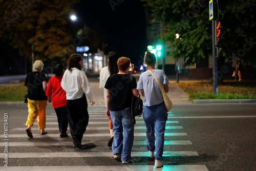 Group of friends walking together at night in a city, crossing the street during a vibrant urban evening
