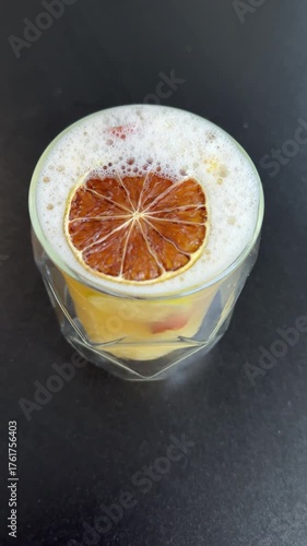 Selective focus on decor of new york sour drink executed in form of orange wheel and dried pink flower on foamy layer. Creative ideas for bartenders for citrus cocktail design complementing.