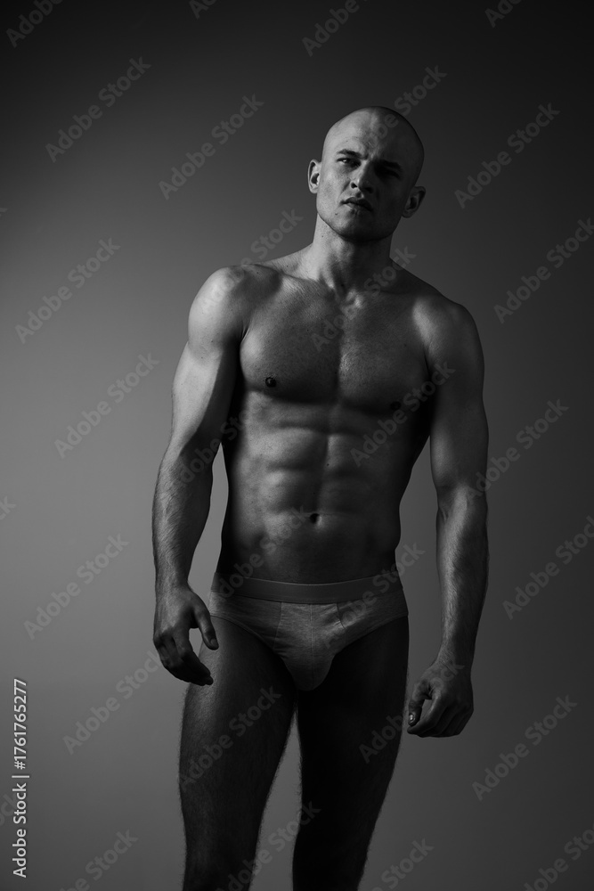 Fototapeta premium Black and white image of a muscular man standing in a confident pose, showcasing athleticism and strength in a minimalistic setting.