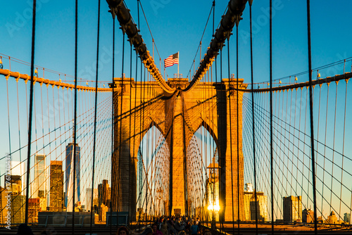 Iconic Brooklyn Bridge Towers Bathed in Golden Sunrise Light, Featuring American Flag and New York City Skyline