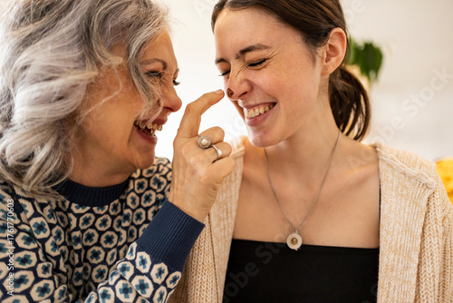 Happy mature woman applying chocolate on daughter's nose