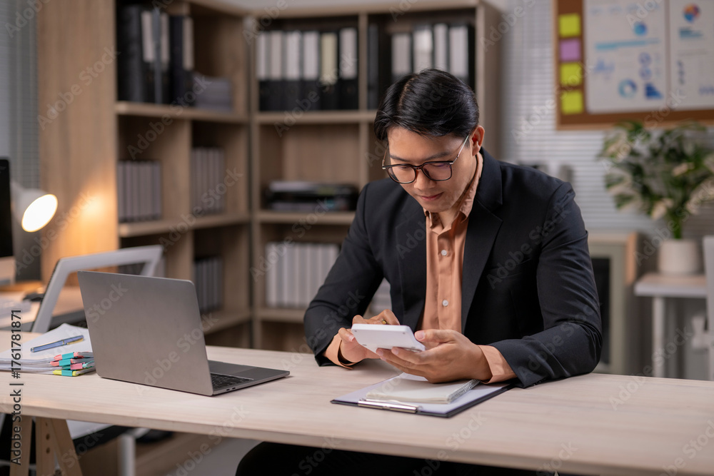 Fototapeta premium A man in a suit is sitting at a desk with a laptop and a calculator