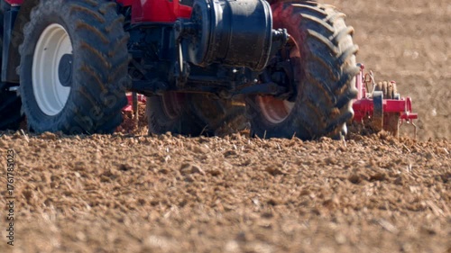 Tractor cultivating dry farmland field with heavy tillage machinery, preparing the soil for the next planting season under bright autumn light.
