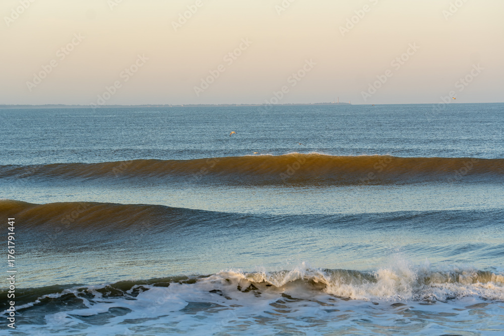 Fototapeta premium Tranquil ocean scene featuring evenly breaking waves under the gentle glow of early morning light. 