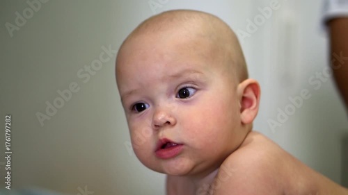 A baby with a blank expression on his face. The baby is wearing a diaper and is laying on his back