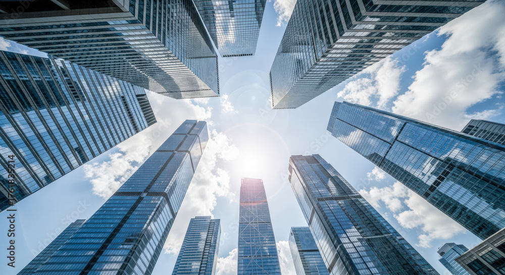 Fototapeta premium Modern skyscrapers in financial district, low angle view of glass office buildings against blue sky with sun flare, business success concept