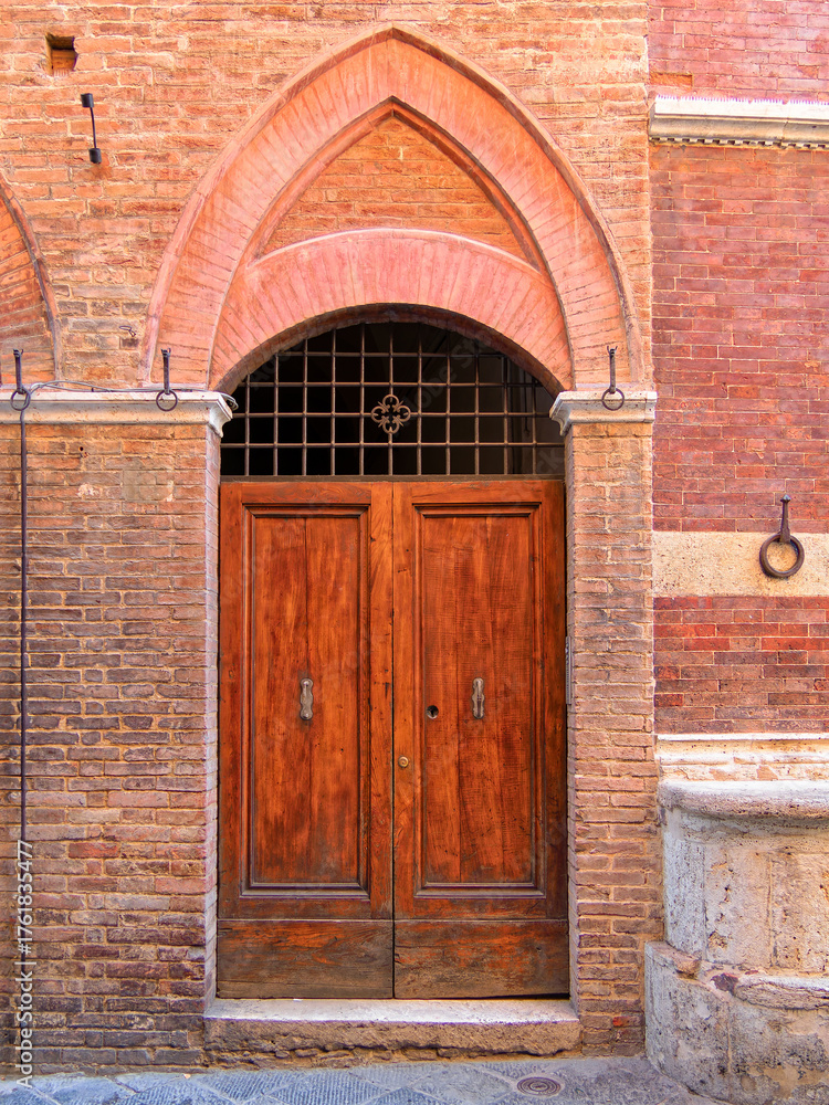 Obraz premium Elegant wooden door within a carved stone archway. The intricate details and textures highlight the region’s architectural charm. Travel to in Siena, Tuscany, Italy.