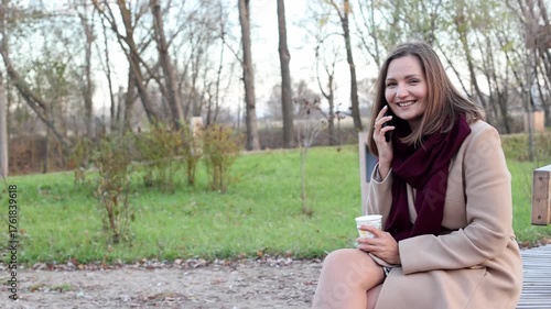 Young attractive woman in the park talking on smartphone and drinking coffee, copy space