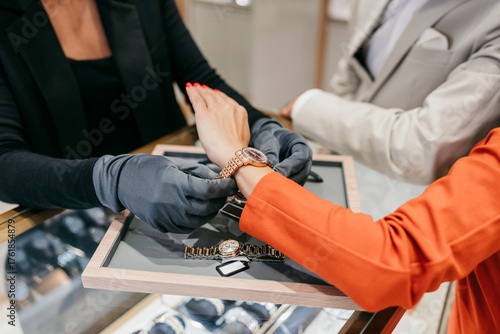 Sales associate in protective gloves assisting a customer with trying on an elegant wrist watch in a luxury jewelry store, offering specialized retail service