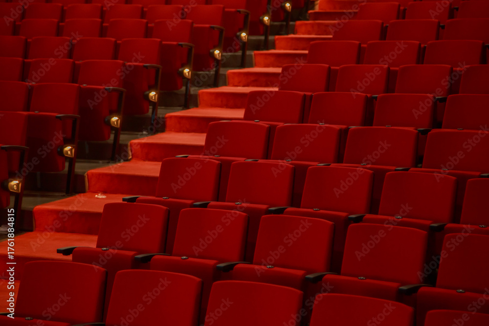 Fototapeta premium Close up view of red theater seats and illuminated aisle inside an empty auditorium