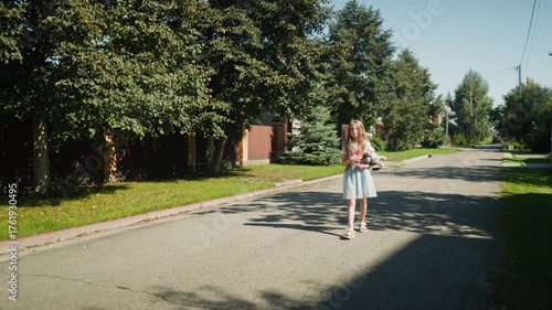 Wallpaper Mural Young girl in light blue dress walks alone along quiet neighborhood street under tree shadows, holding stuffed animal with thoughtful expression in peaceful daytime suburban setting Torontodigital.ca