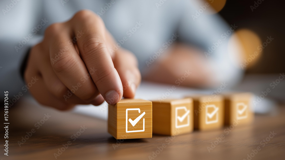 Naklejka premium Hand placing checkmark on wooden blocks with document icons arranged, faceless quality control, review process visualization, defocused desk background, certification symbols detai