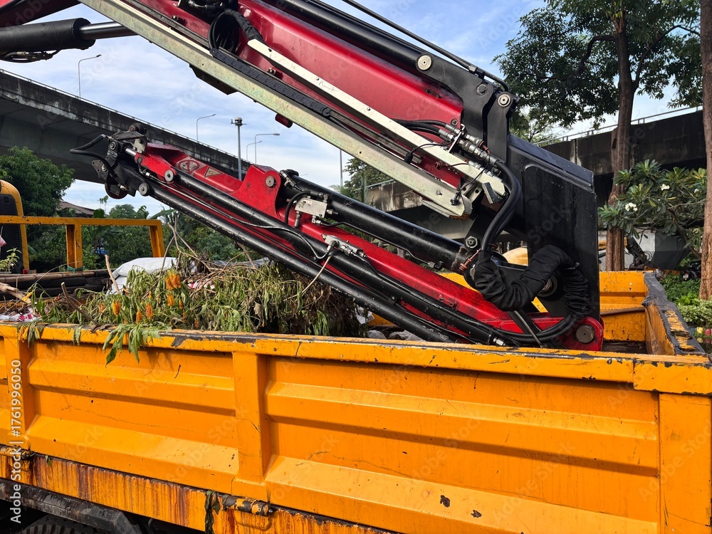Fototapeta premium Truck-mounted crane with hydraulic grapple arm loading debris and green waste onto a dump bed for trash collection and clearing after tree cutting or storm cleanup. Heavy machinery for waste managemen