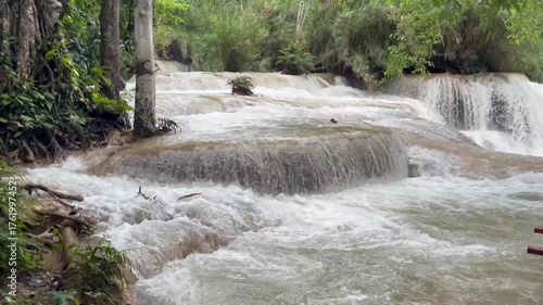 Powerful tropical waterfall flowing through lush green jungle, with foamy white water cascading over rocks. Vibrant natural scenery showing the raw beauty and energy of unspoiled wilderness