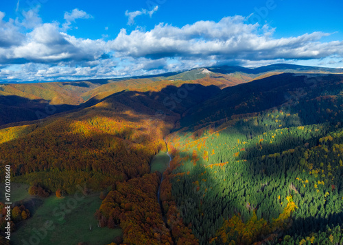 Aerial view with cloud shadows over mountains and forests in autumn. Fall forested mountains seen from above
