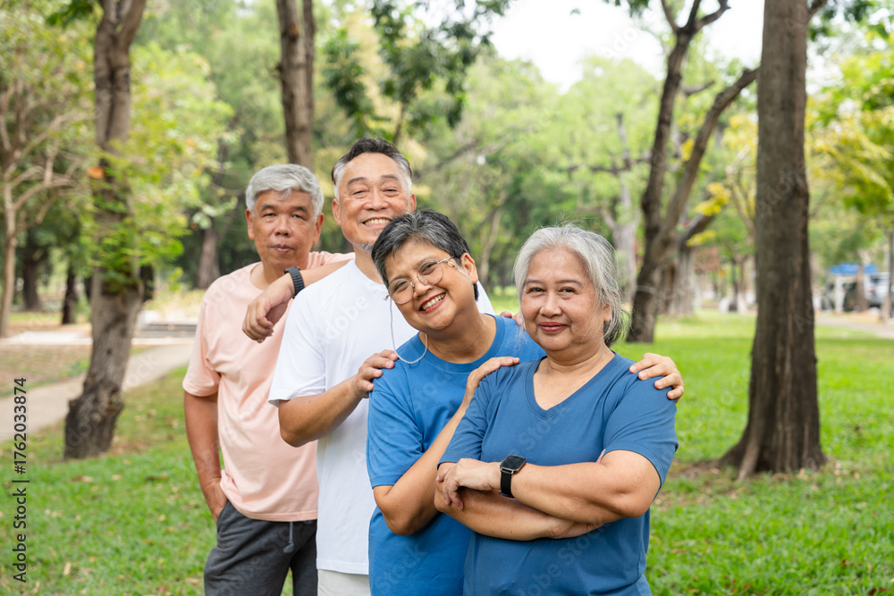 Fototapeta premium Four older adults enjoy a cheerful moment together in a lush outdoor setting. Their smiles and relaxed poses highlight themes of friendship, active aging, and joy of social connection in later life.