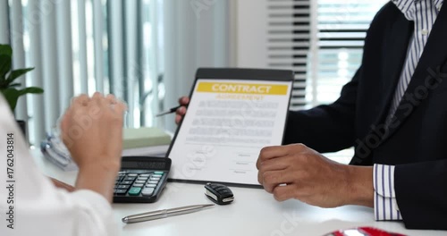 A real estate agent presents a property sale contract to a client, discussing agreement details with a model house on the document, symbolizing home buying, selling, and real estate investment.