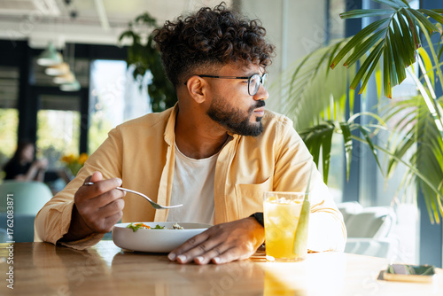 Obraz na plátne Young man eating salad looking away in cafe