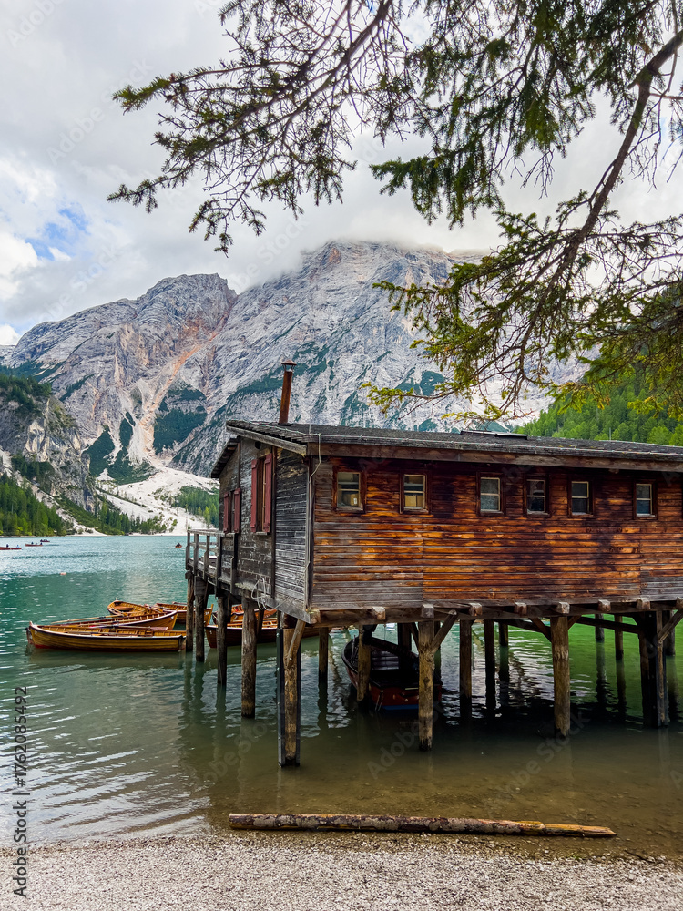 Naklejka premium Lago di Braies or Lake Braies crystal blue lake with wooden rowing boats in Italian Dolomites. Mountain forest lake in Italian alps Dolomites South Tyrol. Woden cabin hut and pontoon above the lake.