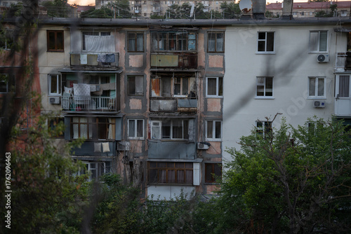 Renovation of the facade of an old panel house. Battered balconies. Sunset in the city. Green trees near the house.