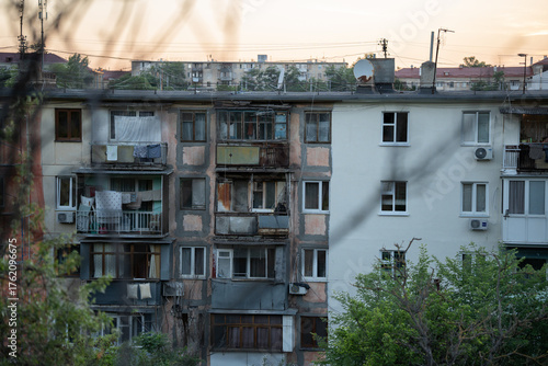 Renovation of the facade of an old panel house. Battered balconies. Sunset in the city. Green trees near the house.