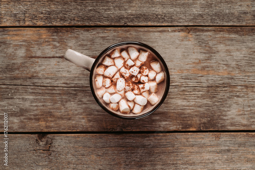 Overhead view of hot chocolate with marshmallows and cocoa powder on rustic background. Winter cozy mood.